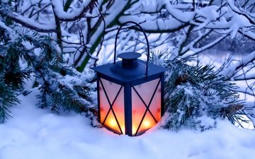 зима, декоративный фонарь с двумя горящими свечами, стоящий на снегу у заснеженной сосновой ветки